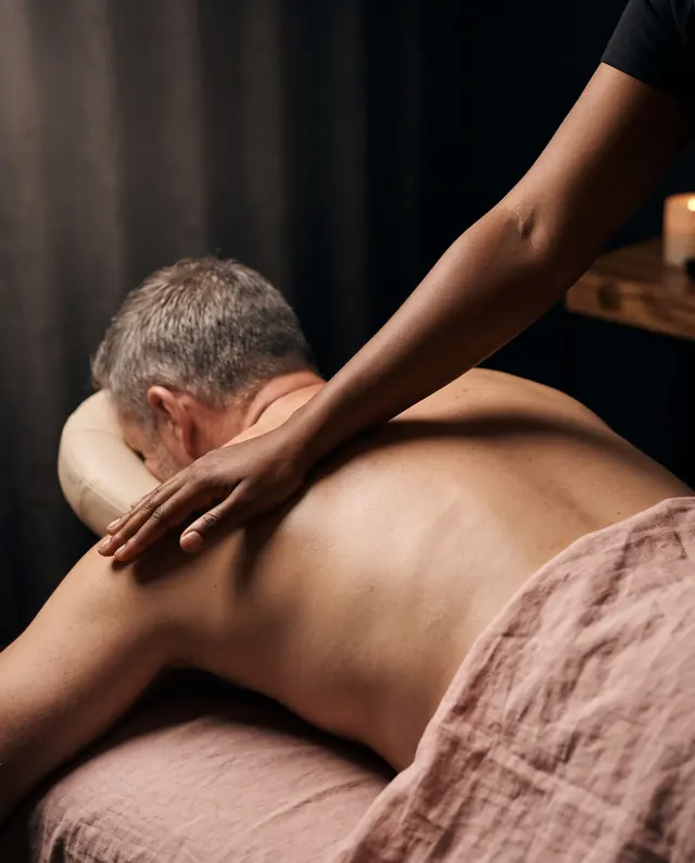 A hand and forearm working slowly into the muscle beside a man's shoulder blade